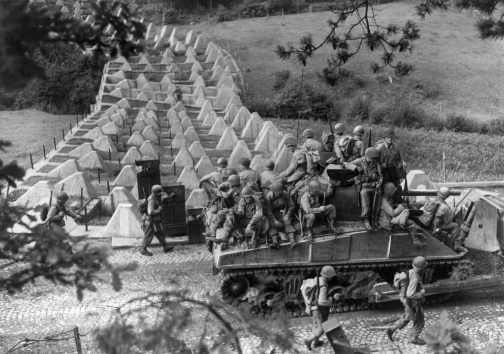 South of Aachen, American soldiers accompanied by an M-4 Sherman tank advance past “dragon’s teeth” tank obstacles on the Siegfried Line. Once inside the city, tanks lost much of the advantage of maneuver and firepower which they utilized in open country. | National Archives